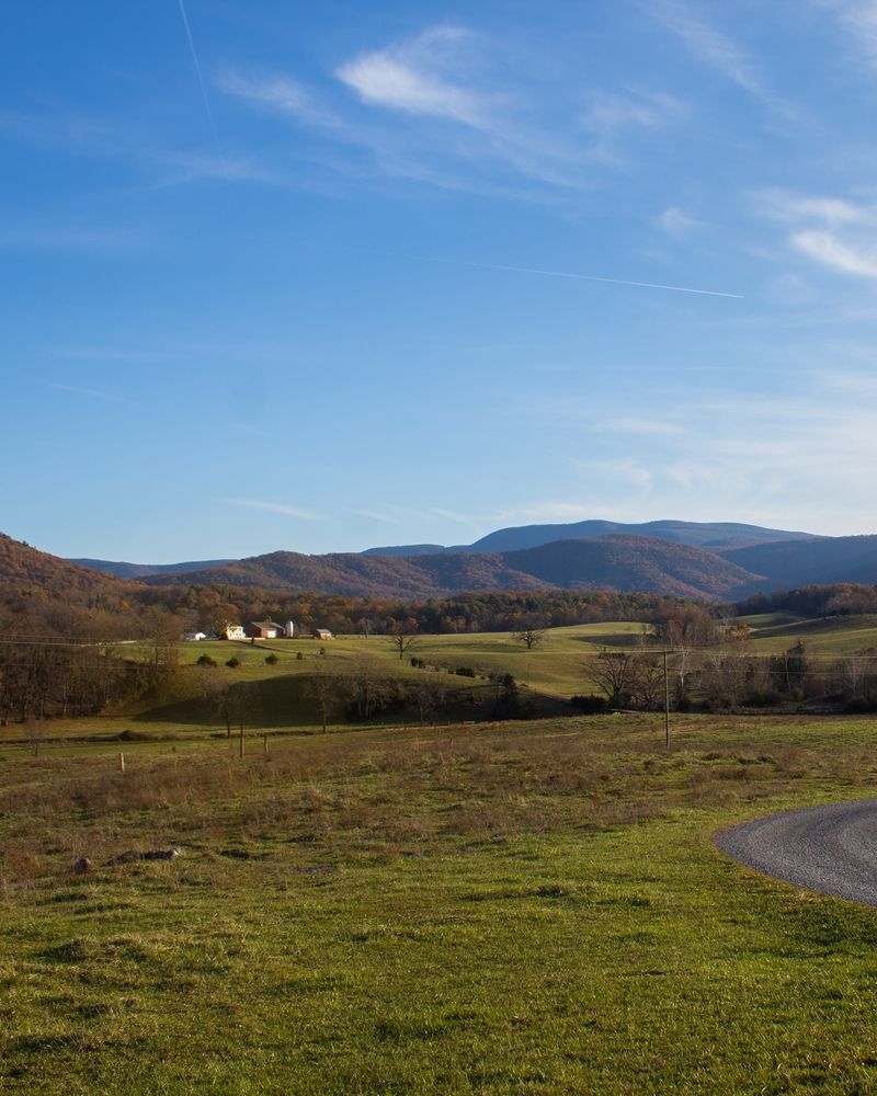A road curving across green pasture toward distant blue hills under a big sky.